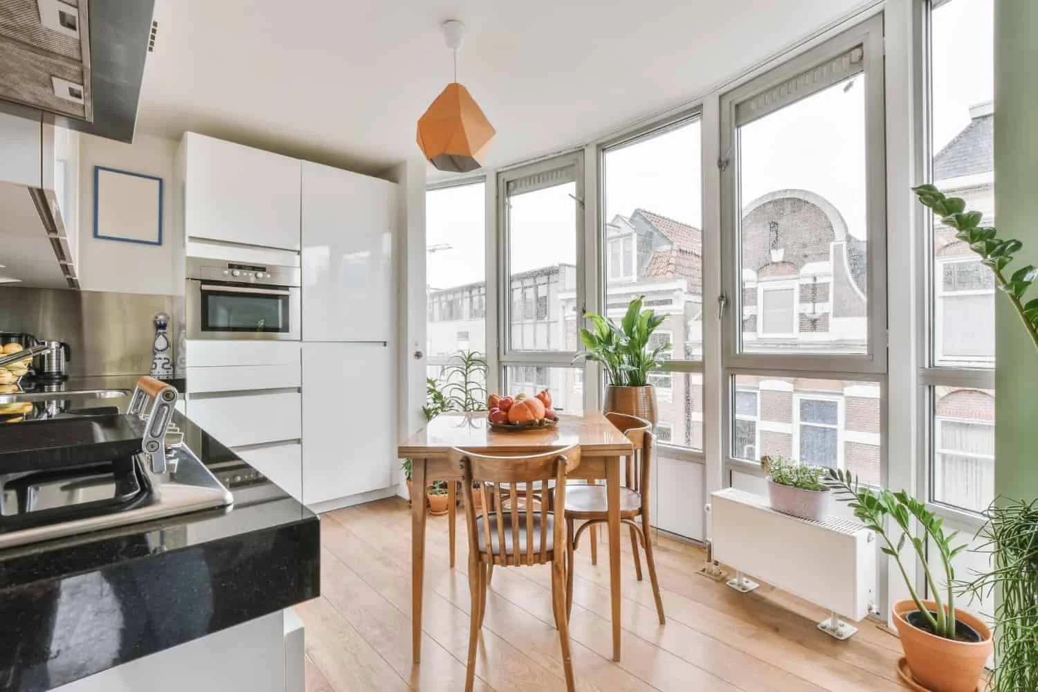 Bucătărie modernă cu mobilier alb lucios, blat negru, zonă de dining și ferestre mari luminoase